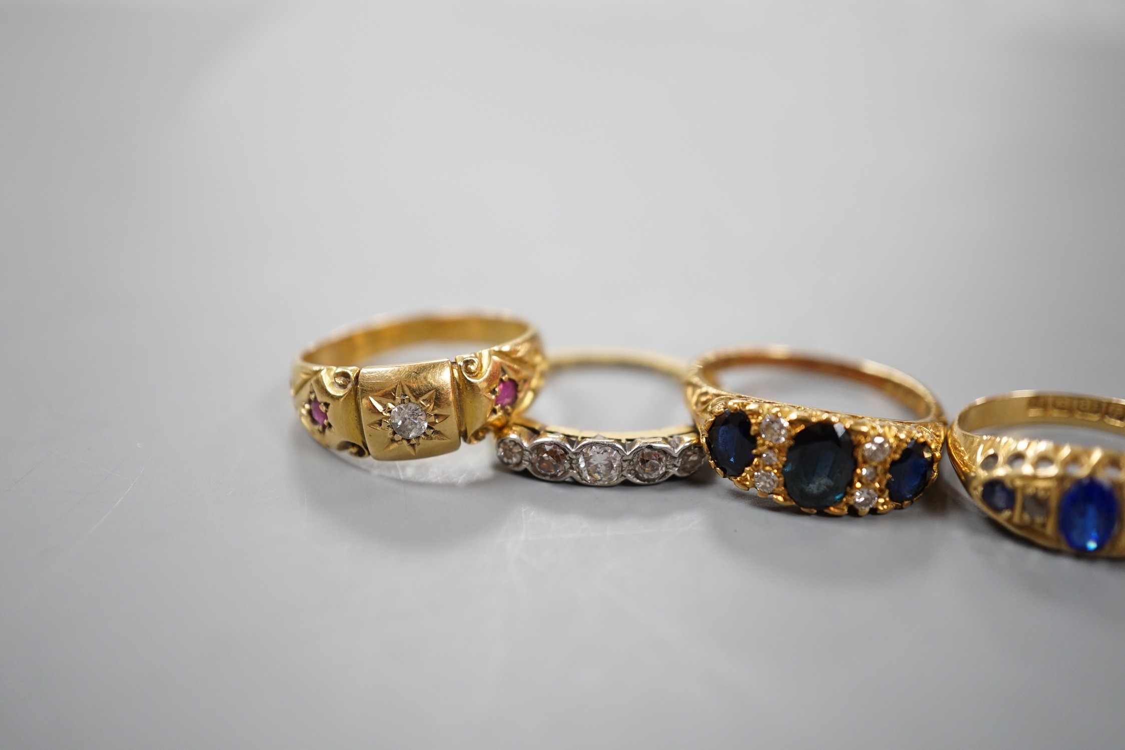 Three early 20th century 18ct and gem set half hoop rings, including ruby and diamond chip, five stone diamond, blue paste and blue stone doublet and diamond chip and a modern 18ct gold sapphire and diamond ring, gross w